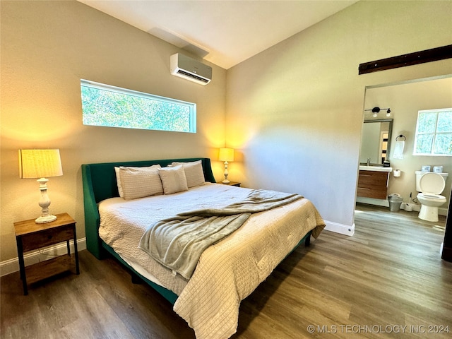 bedroom featuring an AC wall unit, hardwood / wood-style floors, lofted ceiling, and ensuite bathroom