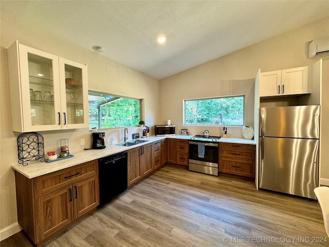 kitchen with appliances with stainless steel finishes, light wood-type flooring, a healthy amount of sunlight, and lofted ceiling