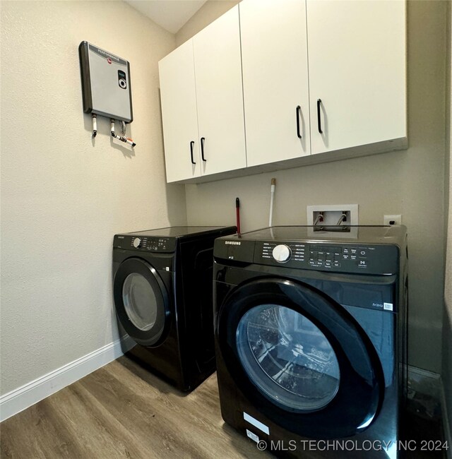 clothes washing area with washer and clothes dryer, light hardwood / wood-style flooring, and cabinets