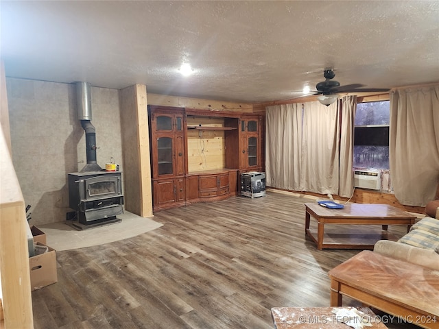 living room with a textured ceiling, cooling unit, a wood stove, ceiling fan, and hardwood / wood-style floors