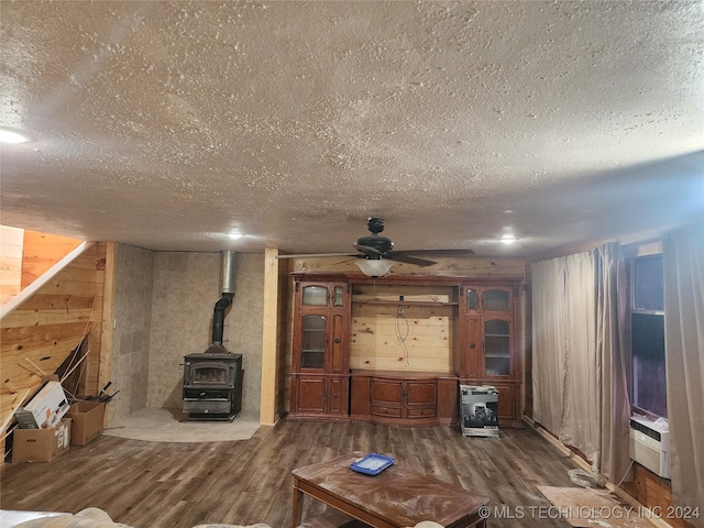 unfurnished living room with a textured ceiling, hardwood / wood-style floors, ceiling fan, wood walls, and a wood stove