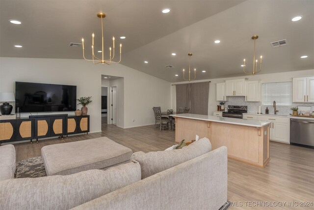 living room with a notable chandelier, light hardwood / wood-style flooring, vaulted ceiling, and sink