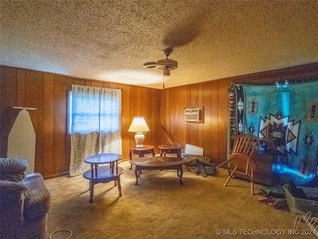 sitting room with ceiling fan, a wall unit AC, wood walls, and light colored carpet