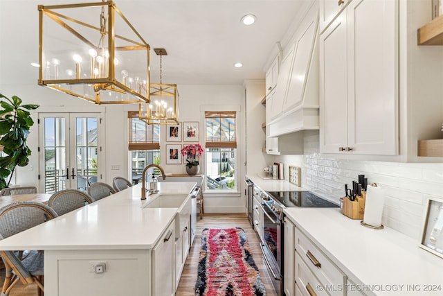 kitchen with premium range hood, decorative backsplash, stainless steel range with electric stovetop, light wood-type flooring, and an island with sink