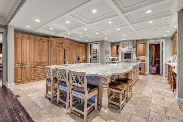 kitchen featuring sink, a spacious island, wall chimney exhaust hood, coffered ceiling, and light tile patterned floors