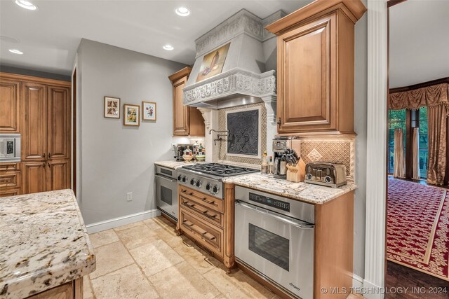 kitchen with backsplash, stainless steel appliances, light stone counters, light tile patterned floors, and custom exhaust hood