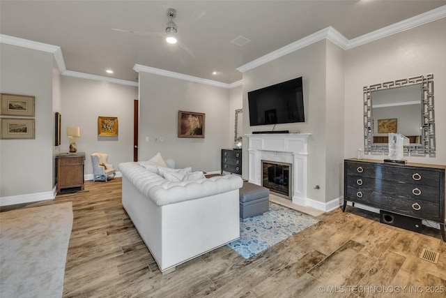 living area with a premium fireplace, baseboards, wood finished floors, and ornamental molding