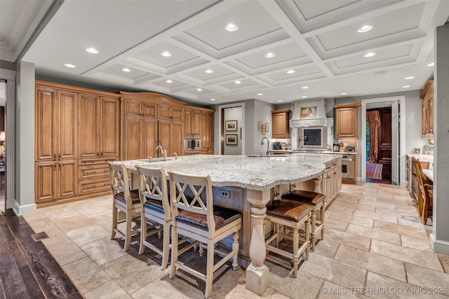 kitchen featuring stone tile floors, brown cabinetry, a large island, custom exhaust hood, and a sink