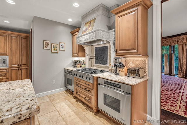 kitchen featuring tasteful backsplash, stone tile floors, light stone countertops, custom exhaust hood, and stainless steel appliances