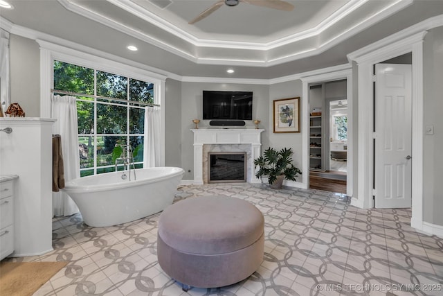 bathroom with a high end fireplace, a freestanding bath, tile patterned floors, a raised ceiling, and crown molding