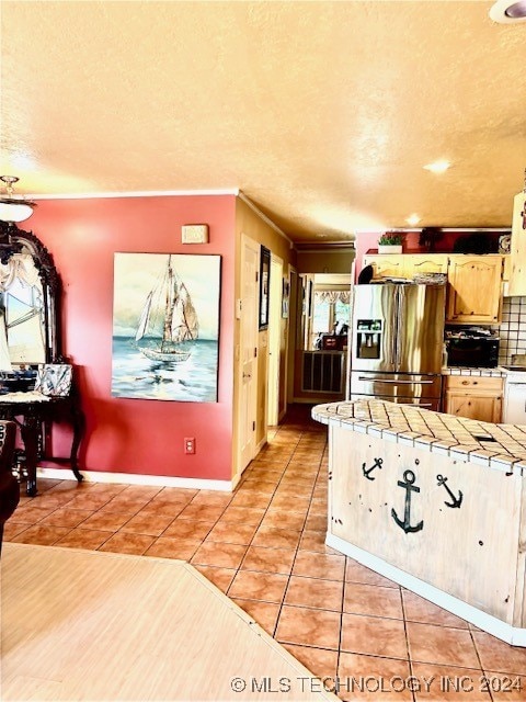 kitchen featuring crown molding, light tile patterned floors, stainless steel fridge with ice dispenser, tile countertops, and tasteful backsplash