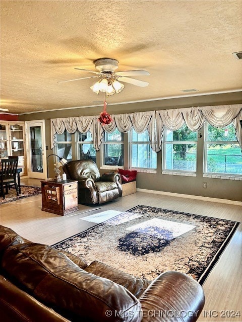 living room featuring ceiling fan, wood-type flooring, a textured ceiling, and a healthy amount of sunlight