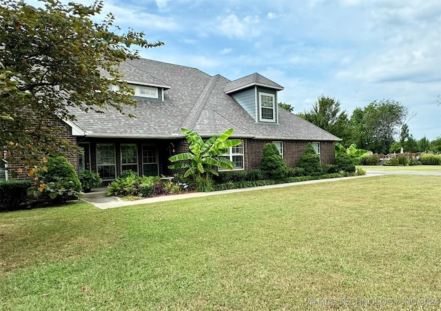 view of front of home with a shingled roof, a front yard, and brick siding