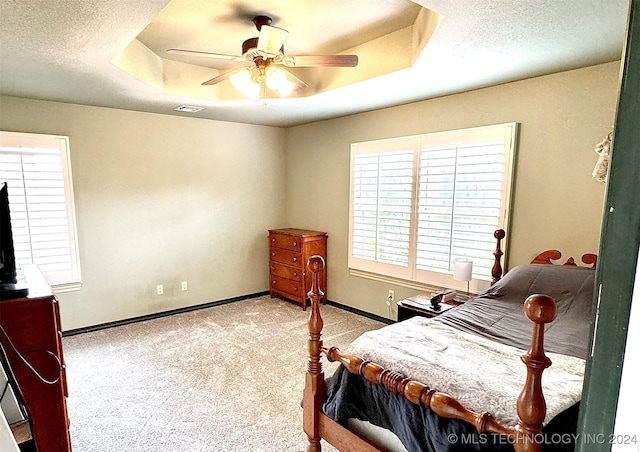 bedroom featuring a tray ceiling, visible vents, light carpet, a textured ceiling, and baseboards