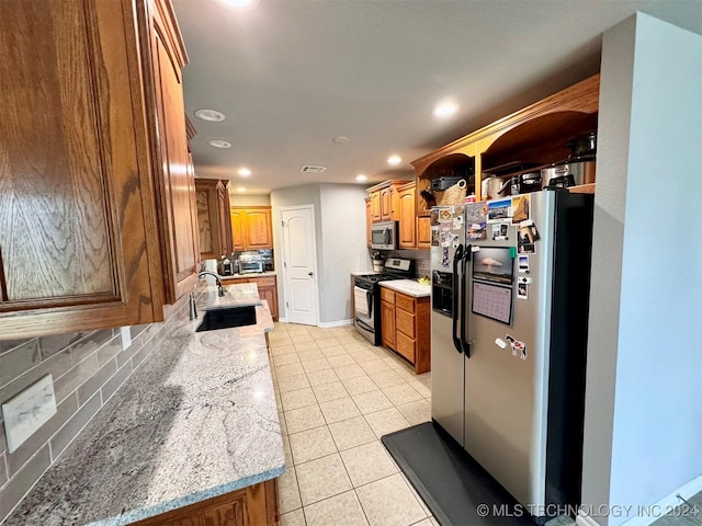 kitchen featuring brown cabinets, light tile patterned floors, tasteful backsplash, appliances with stainless steel finishes, and a sink