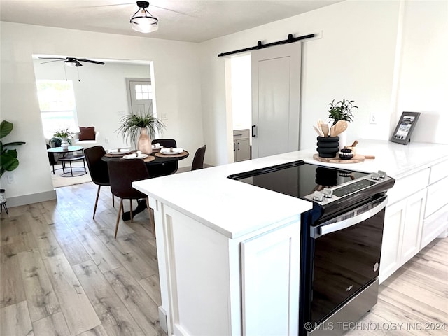 kitchen featuring electric range, ceiling fan, light hardwood / wood-style flooring, white cabinets, and a barn door