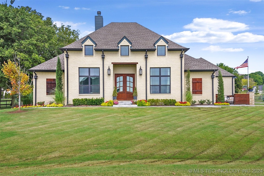 french country style house featuring french doors, brick siding, a chimney, and a front lawn