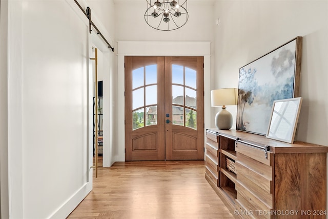 entrance foyer with light hardwood / wood-style flooring, french doors, a barn door, and a chandelier