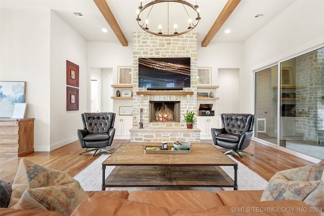 living room with beamed ceiling, light hardwood / wood-style flooring, a chandelier, and a stone fireplace