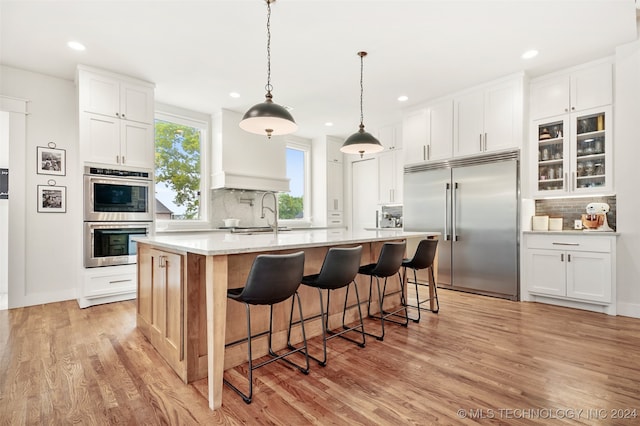 kitchen featuring backsplash, light hardwood / wood-style flooring, fridge, and multiple ovens