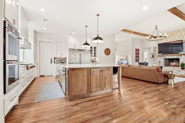 kitchen featuring a center island with sink, stainless steel appliances, light hardwood / wood-style floors, beam ceiling, and white cabinets