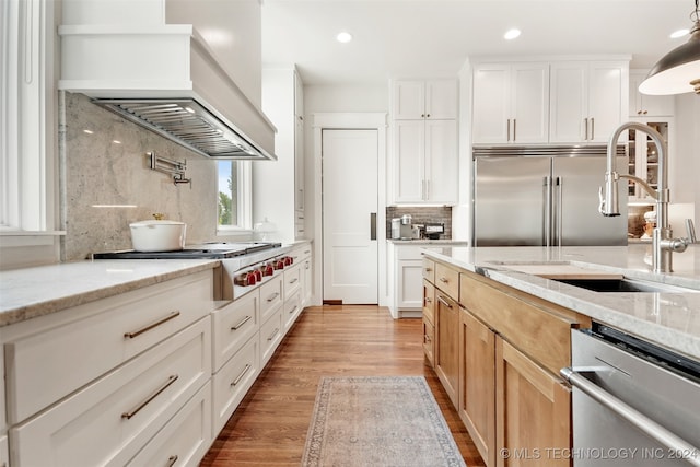 kitchen featuring decorative backsplash, appliances with stainless steel finishes, light stone countertops, light wood-type flooring, and premium range hood