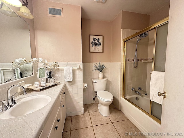 full bathroom with toilet, bath / shower combo with glass door, tile walls, vanity, and tile patterned floors