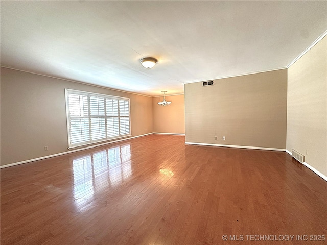 spare room featuring dark wood-type flooring, ornamental molding, and an inviting chandelier