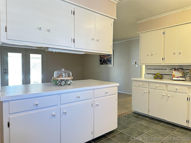 kitchen with crown molding, white cabinets, wooden walls, and dark tile patterned floors