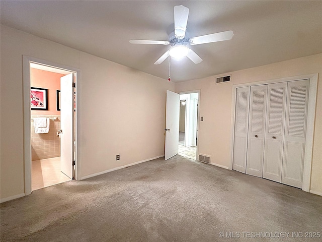 unfurnished bedroom featuring ceiling fan, light colored carpet, a closet, and ensuite bath