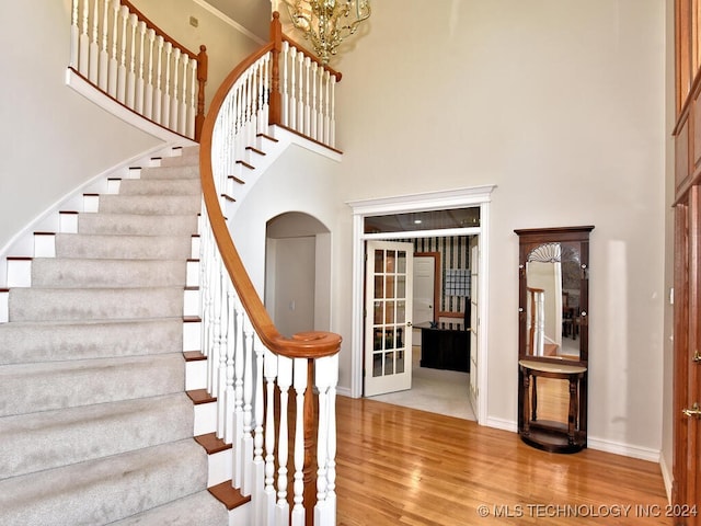 staircase featuring french doors, a high ceiling, a chandelier, and hardwood / wood-style floors