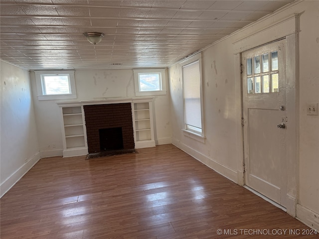 unfurnished living room featuring wood-type flooring, plenty of natural light, and built in shelves