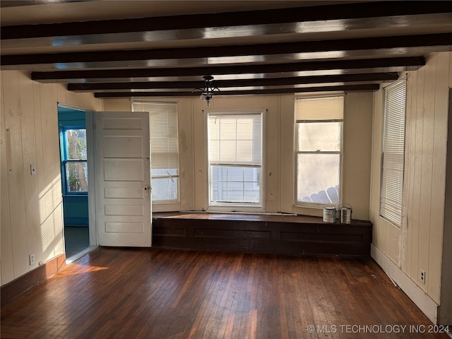 unfurnished room with beamed ceiling, a wealth of natural light, wooden walls, and dark hardwood / wood-style floors