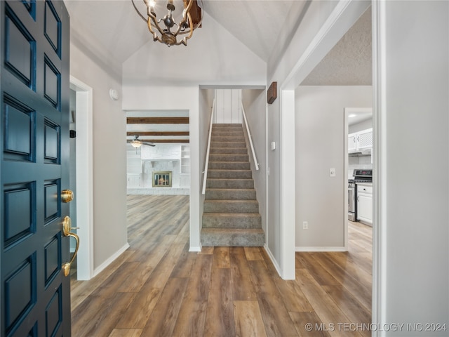 entrance foyer featuring ceiling fan with notable chandelier, lofted ceiling with beams, hardwood / wood-style flooring, and a stone fireplace