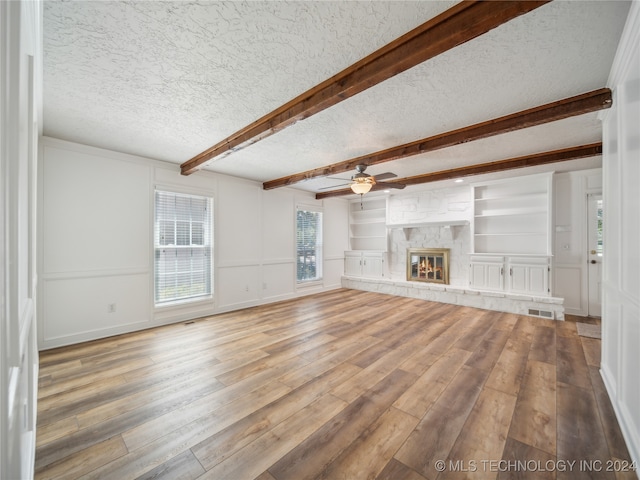 unfurnished living room featuring a fireplace, hardwood / wood-style floors, a textured ceiling, and built in features