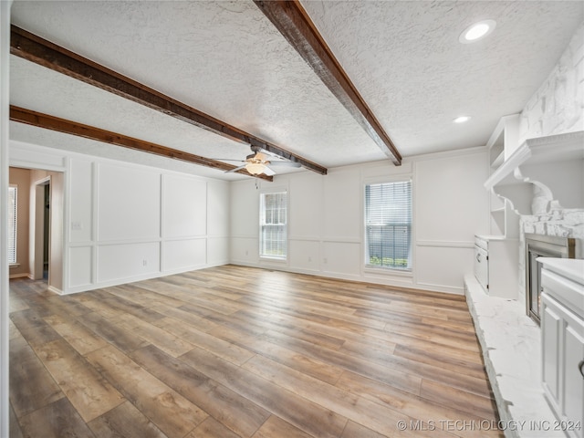 unfurnished living room featuring ceiling fan, a fireplace, a textured ceiling, beamed ceiling, and light hardwood / wood-style floors