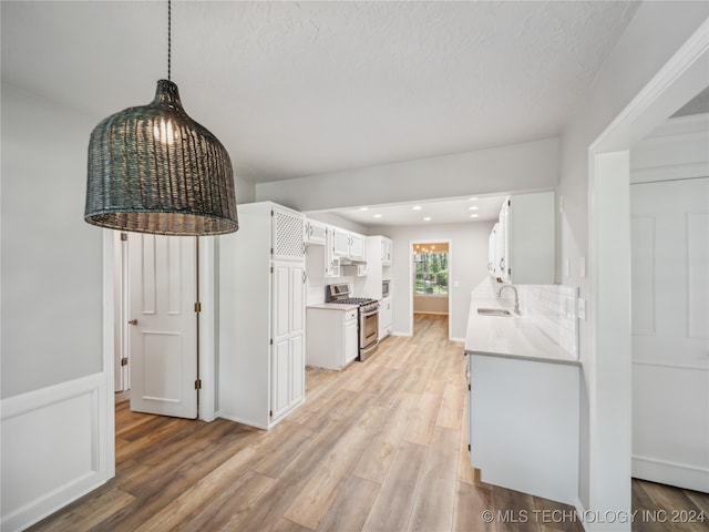 kitchen with stainless steel gas stove, sink, light hardwood / wood-style flooring, pendant lighting, and white cabinets