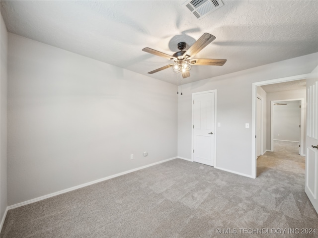 unfurnished bedroom with ceiling fan, light carpet, and a textured ceiling