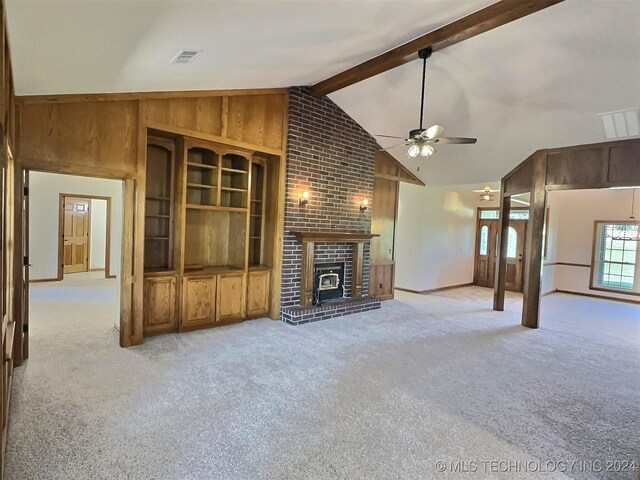 unfurnished living room featuring a fireplace, light carpet, wooden walls, beamed ceiling, and ceiling fan