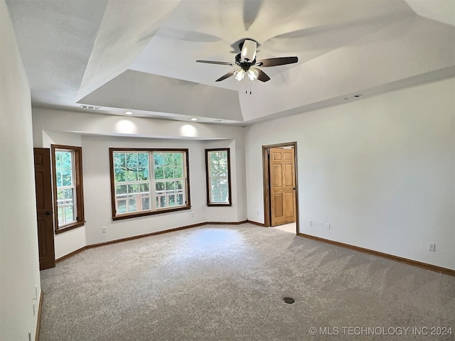 empty room featuring ceiling fan, a raised ceiling, and light carpet