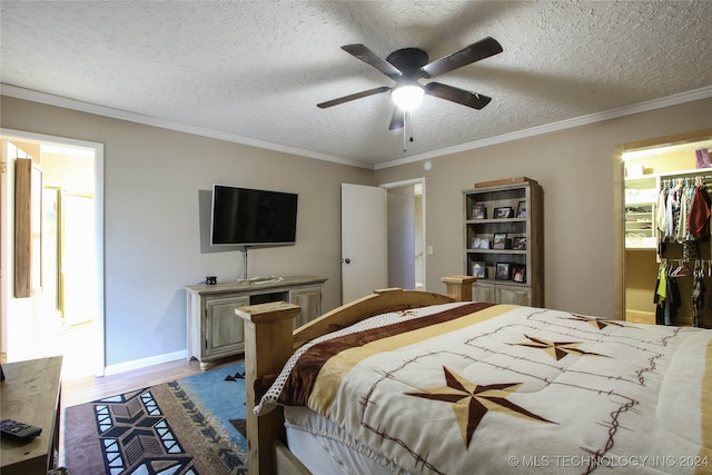 bedroom featuring a spacious closet, ornamental molding, ceiling fan, and a textured ceiling