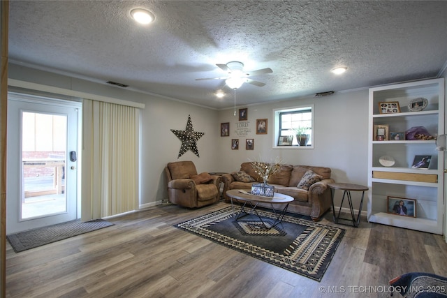 living room featuring built in shelves, wood-type flooring, a textured ceiling, ornamental molding, and ceiling fan