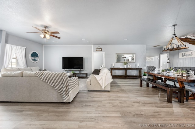 living room featuring ceiling fan with notable chandelier, a textured ceiling, and light wood-type flooring