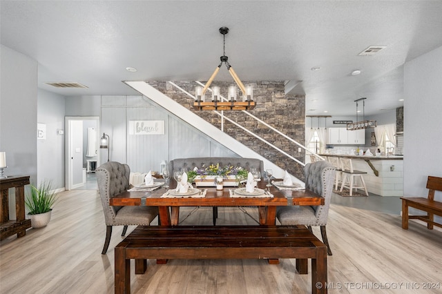 dining space with light hardwood / wood-style floors, a textured ceiling, and a notable chandelier