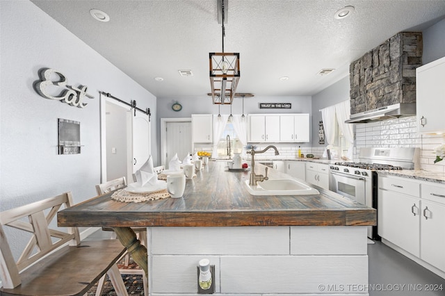 kitchen featuring a breakfast bar, an island with sink, white cabinets, gas range, and a barn door