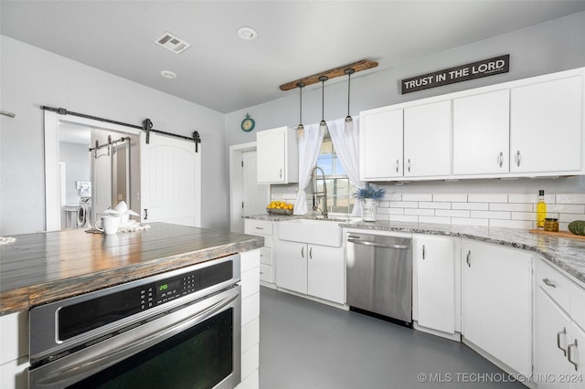 kitchen with appliances with stainless steel finishes, decorative light fixtures, sink, white cabinets, and a barn door