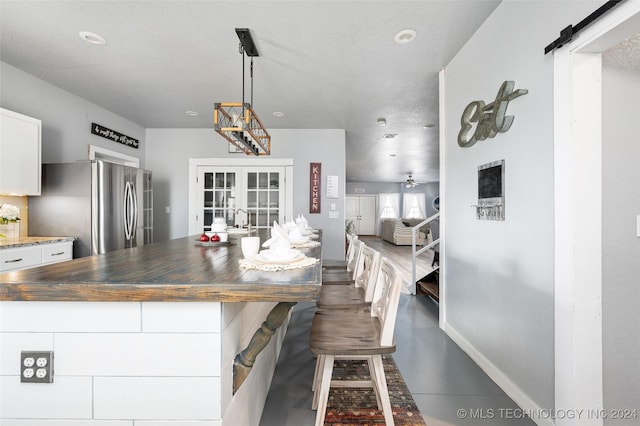 kitchen featuring stainless steel refrigerator, decorative light fixtures, white cabinets, a barn door, and french doors