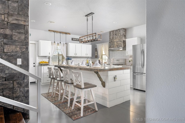 kitchen featuring stainless steel refrigerator, tasteful backsplash, white cabinetry, a kitchen bar, and hanging light fixtures