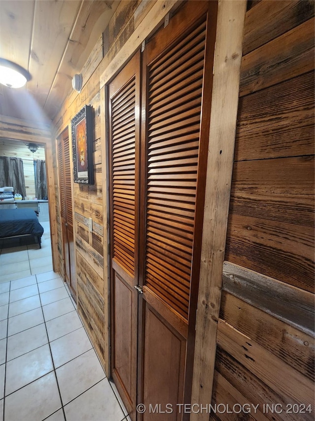 corridor with lofted ceiling, wooden walls, and light tile patterned flooring