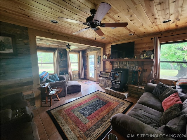 living area with wooden walls, wooden ceiling, ceiling fan, a wood stove, and tile patterned flooring